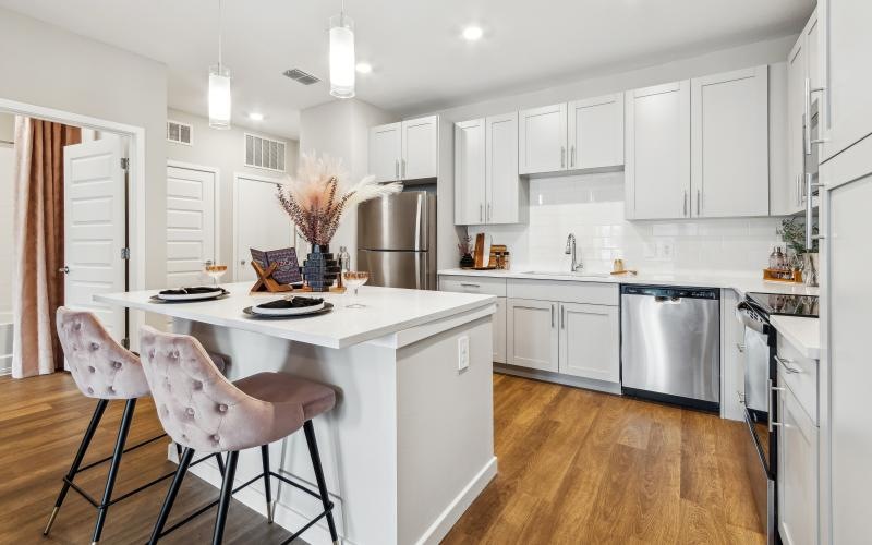 a kitchen with white cabinets and dishwasher and white island with seating